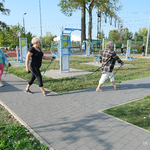 Otwarta przestrzeń siłowni pod chmurką przy ul. Szkolnej. Uczestniczki zajęć sportowych spacerują z kijkami do nordic walking.