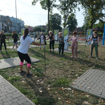 Otwarta przestrzeń siłowni pod chmurką przy ul. Szkolnej. Uczestniczki zajęć sportowych ćwiczą naśladując instruktorkę.