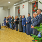 Goście specjalni spotkania stoją obok siebie przy ścianie słuchając kolędy. 