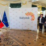 Prezydent Białegostoku mówi do mikrofonu. Uczestnicy konferencji stoją w pobliżu ścianki z logo Miasta Białystok.