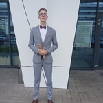 Chodnik przed budynkiem. Jakub pozuje do zdjecia z otrzymaną nagrodą.